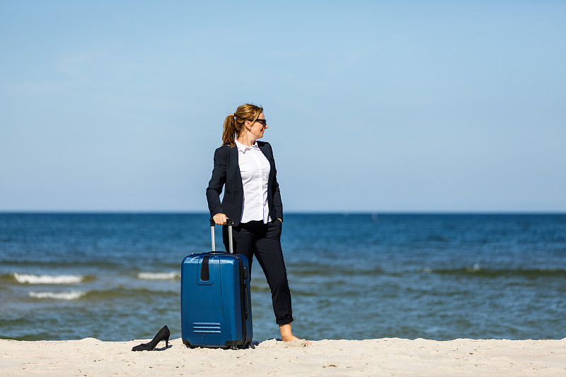 女商人提着旅行箱站在海边