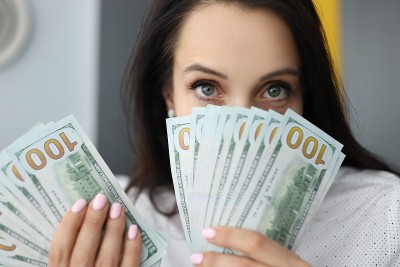 年轻的女商人手里拿着许多美元，遮住了脸