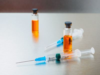 特写注射注射器和安瓿与橙色冠状病毒疫苗在银色铝背景。