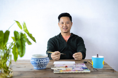 一位亚洲男性艺术家用毛笔和水彩调色板在纸上作画