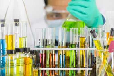 实验室玻璃试管和化学瓶与彩色的化学溶液和人类科学家看绿色的化学溶液在厄伦迈耶烧瓶作为背景