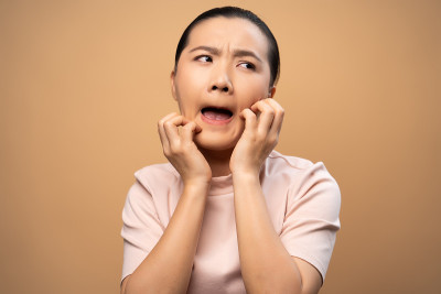 亚洲妇女是刺激物瘙痒她的皮肤孤立站在米色背景。
