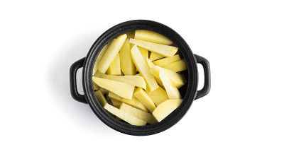 几片生土豆放在一个黑色的锅里，孤立在白色的背景上