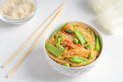 韩国Japchae素食沙拉，玻璃面条，青豆和豆荚与筷子和芝麻在白色木制背景