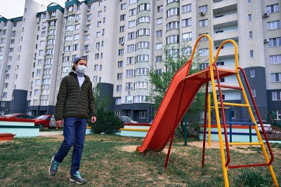 一名十几岁的男孩走过高楼大厦附近的操场，这是一个居民区，他脸上戴着医用口罩，防止病毒和灰尘