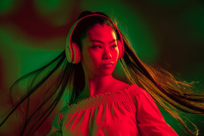 年轻的亚洲女孩戴着耳机孤立在红绿霓虹灯背景下。