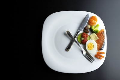 一个模拟时钟的盘子，叉子和刀的指针显示食物，间歇性禁食的概念