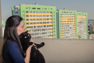 一个带着黑猫的女孩从阳台看向一座新楼