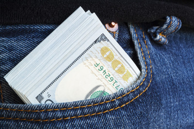 大叠百元钞票从牛仔裤的口袋里凸出来。现金贿赂的概念。所有挣来的钱都是为了荣誉。