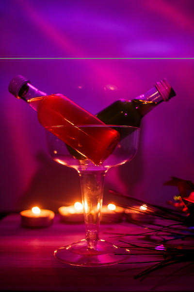 红色和绿色酒瓶子在鸡尾酒杯与粉红色LED背景在俱乐部设置蜡烛火焰