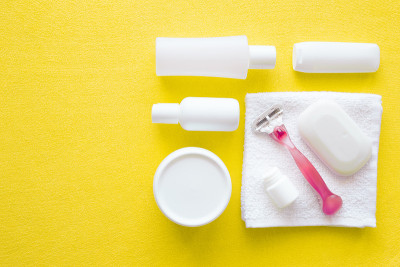 女人剃须刀和黄色毛巾上的白色美容洗漱用品不同。每天剃须。光滑的皮肤。用软面霜护理身体。文字或标识的空