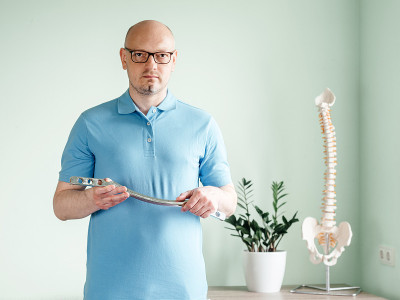 一名男性整骨医师，手持用于软组织治疗的不锈钢IASTM治疗工具，工具辅助软组织移动和最终筋膜松解