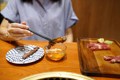 手握筷子挑出烤和牛肉，蘸上腌蛋黄酱。
