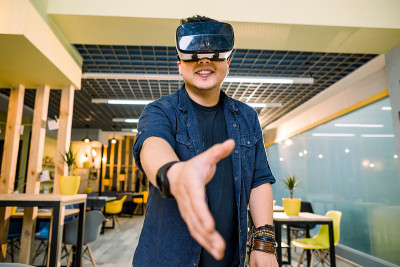 年轻的中国商人戴着虚拟现实眼镜在办公室工作。在增强现实中使用VR头盔握手的人