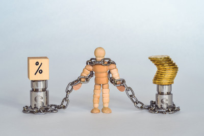 一个用木头制成的人用链子绑在金属重物上，象征着美元、硬币和利息。
