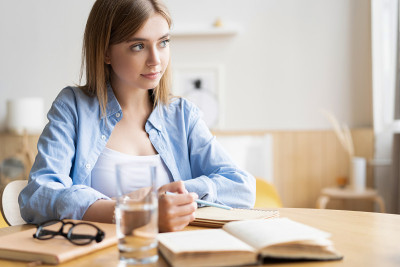 专注的年轻女子在家里的桌子上写信。专注的女商人在笔记本上做笔记
