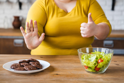 爱沉思的肥胖白人女性选择健康的食物而不是甜食。节食的概念。很难在健康的生活方式和不良的饮食习惯之间做