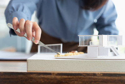 在建筑工作室中，建筑师女性用镊子在现代家庭模型上制作一个模拟灌木，建筑设计师或建筑师学生概念