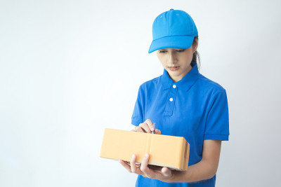 年轻的亚洲女人和穿制服的快递员。女人拿着盒子迷人的微笑孤立在白色的背景。