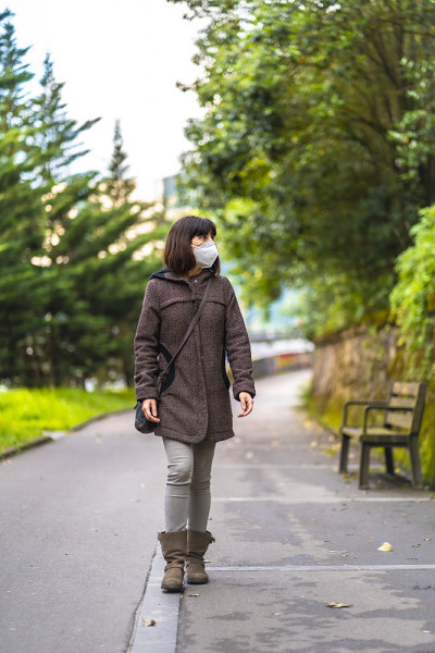 一个留着短发戴着面具的白人黑发女人在公园里散步。首次接触未受控制的Covid-19大流行
