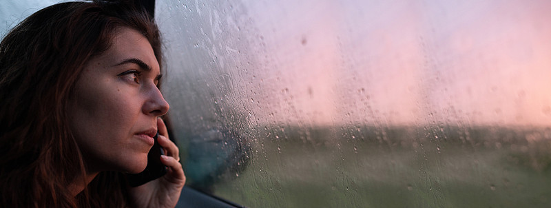 下着雨，一名年轻女子在车里打电话。