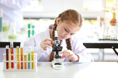 快乐的小女孩用显微镜做科学实验(教育和科学概念)
