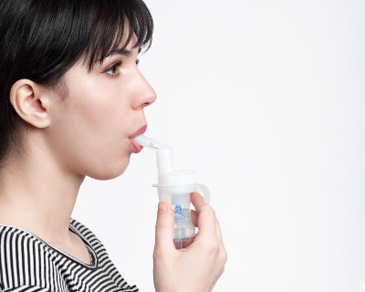使用吸入器的黑发女人的侧面图片。病人吸入药物
