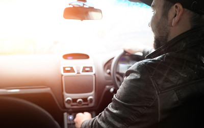 一个男人开车。司机正开着汽车沿路行驶。太阳使开车的人看不见。