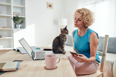 在家用笔记本电脑工作的女性，身边有一只宠物猫。