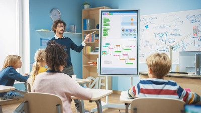 小学计算机科学教师使用交互式数字白板向满教室的聪明多样化的孩子展示编程逻辑。让孩子们听计算机课