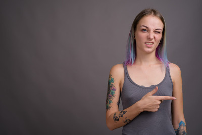 工作室拍摄的年轻美丽的女人与多颜色的头发和纹身穿着灰色背心对灰色背景