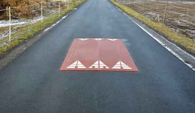 在通往居民区的道路中间，警察和交通办公室安装了一个红色塑料减速机。侧面有斜面的橡胶制成的凸起的方形物