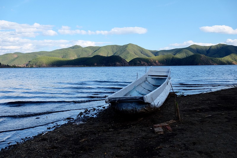 一条白色的船搁浅在黑土海滩上。蓝色的湖波。青山的背景。晴朗的蓝天。