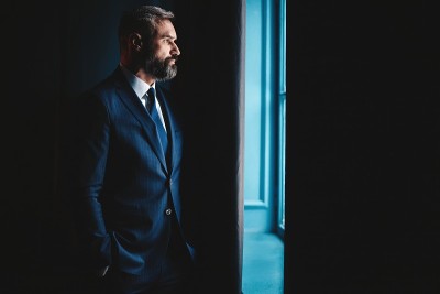 思考……穿着全套西装的体贴男人站在室内，透过窗户向外看。