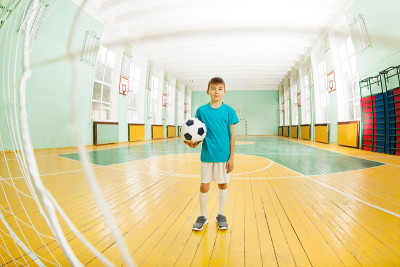 一个男孩拿着足球站在学校体育馆里