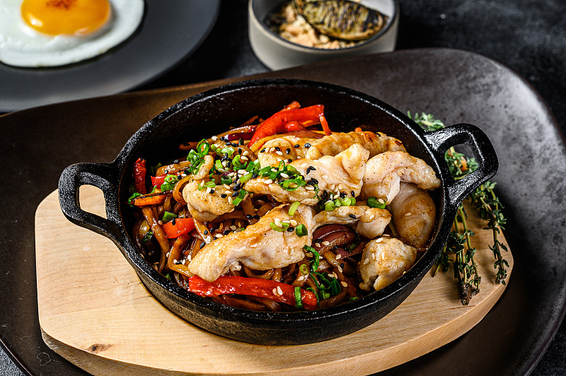 乌冬面与鸡肉和蔬菜在平底锅中煸炒。黑色背景。俯视图