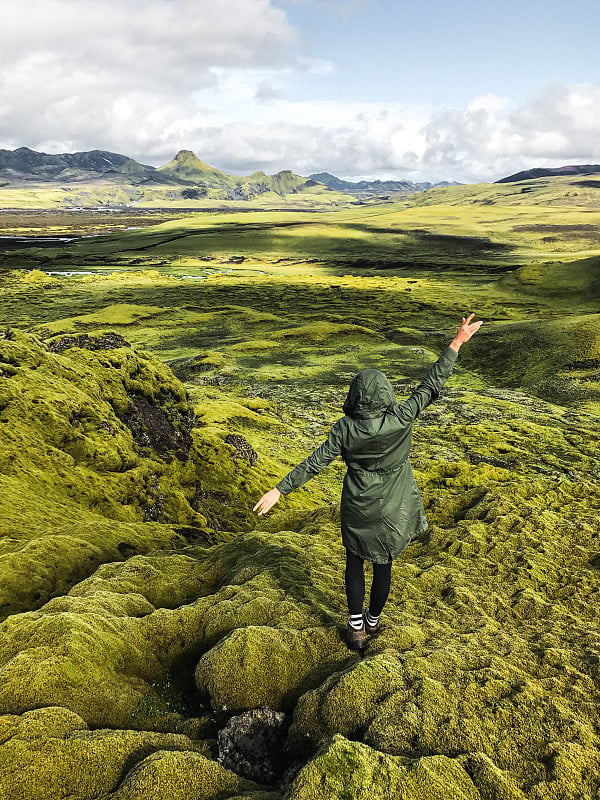 年轻平静的女人欣赏着冰岛覆盖着苔藓的草地。北极圈野生自然。人与自然的联系。女性穿着舒适的防水绿色皮大