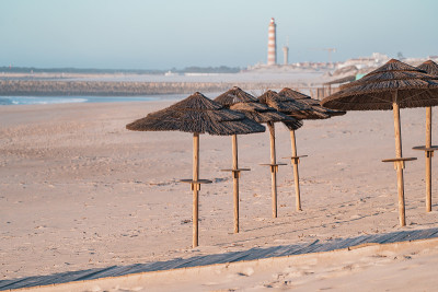 日落时分，海滩上的草棚撑着遮阳伞，普拉亚·达·巴拉灯塔(Lighthouse of Praia da