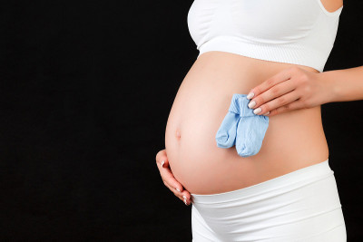 一个穿着白色内衣的孕妇在黑色背景下抱着蓝色袜子给一个男婴的特写。未来儿童期望概念。本空间