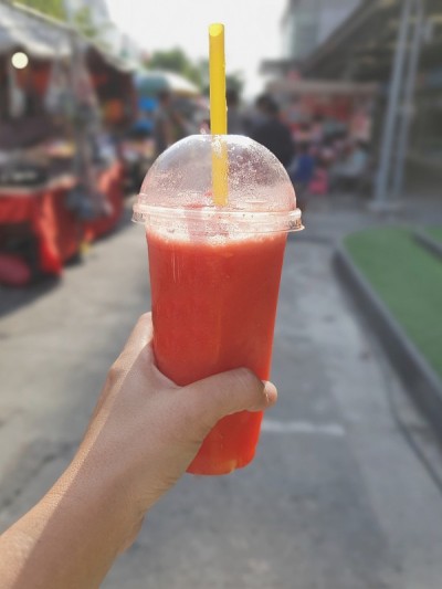 用塑料玻璃杯盛着草莓奶昔，以街头小吃为背景
