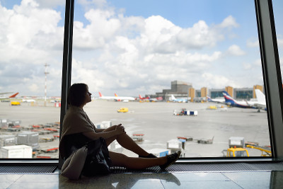 一个背着背包、抱着旅游枕头的女人坐在候机室的窗口看飞机。