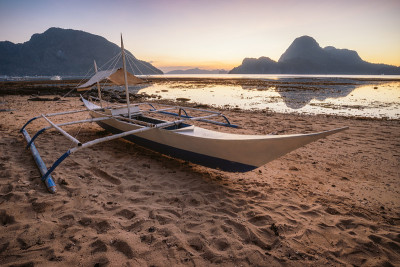 菲律宾巴拉望省。埃尔尼多海岸海滩与当地班卡船与风景如画的日落，金色的光风景和岛屿形状的背景