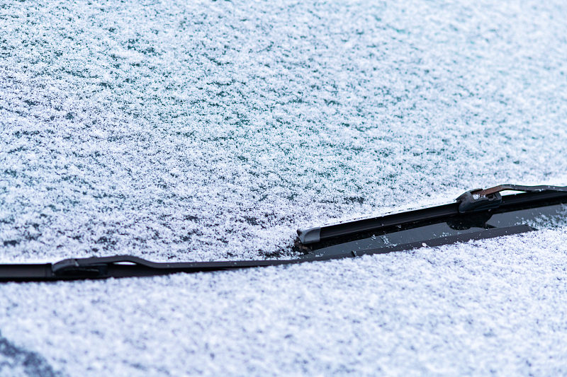 雪覆盖了车窗，用雨刷，微距，特写。没有使用防冻液。车辆在雪。冬天来了。恶劣的天气条件