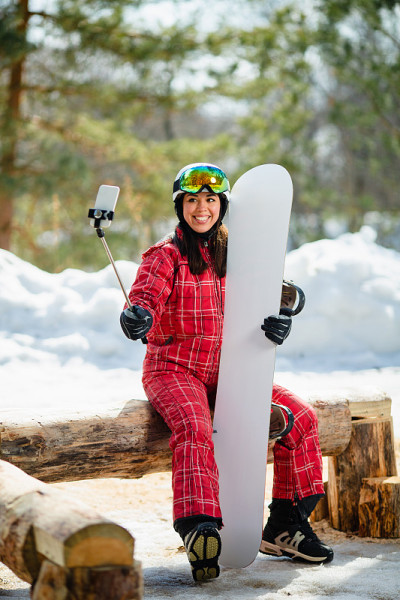 一名女子拿着滑雪板，把智能手机放在棍子上自拍