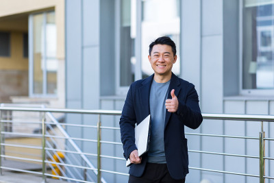 肖像英俊的亚洲人大学学院教师，商人，科学家或教育家。站在现代办公中心或校园背景，双臂交叉站在户外，对