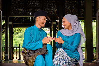年轻夫妇马来穆斯林在传统服装握手在Aidilfitri庆祝传统木屋。