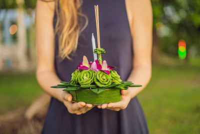 一名女游客手里拿着Loy Krathong，准备把它扔进水里。泰国的水牛节，人们购买鲜花和蜡烛点亮并