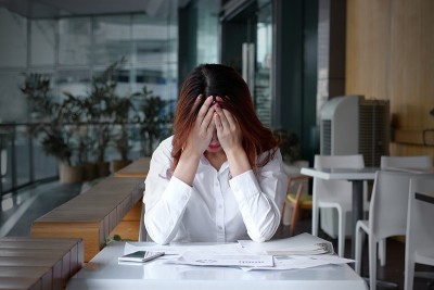 正面视图的压力沮丧的年轻亚洲商业妇女覆盖脸与手在办公室的桌子上