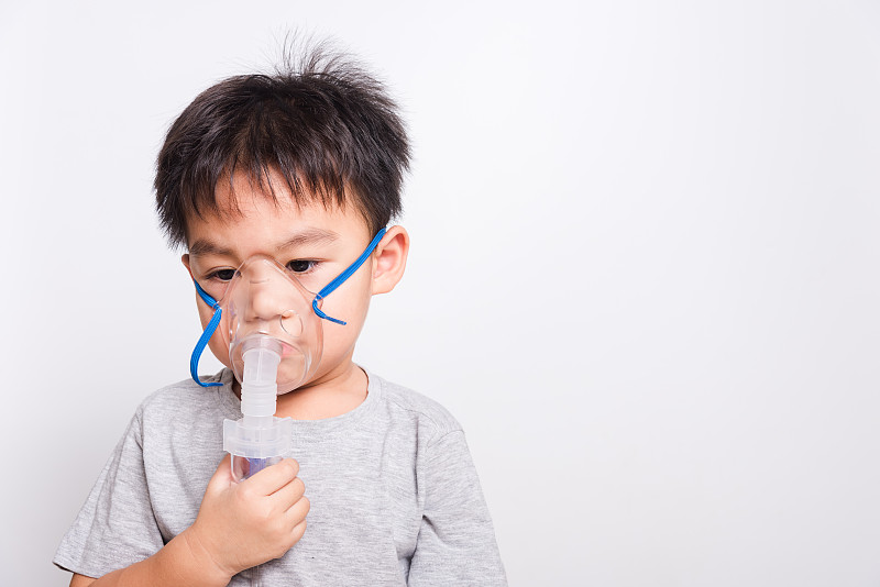 特写亚洲脸，生病的小孩他用蒸汽吸入器雾化面罩吸入自己的白色背景
