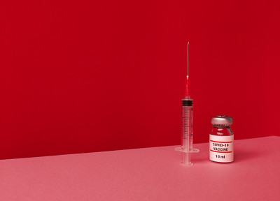 带有covid - 19疫苗和注射器的医疗瓶，红色背景，倾斜的时尚天际线和拷贝空间。